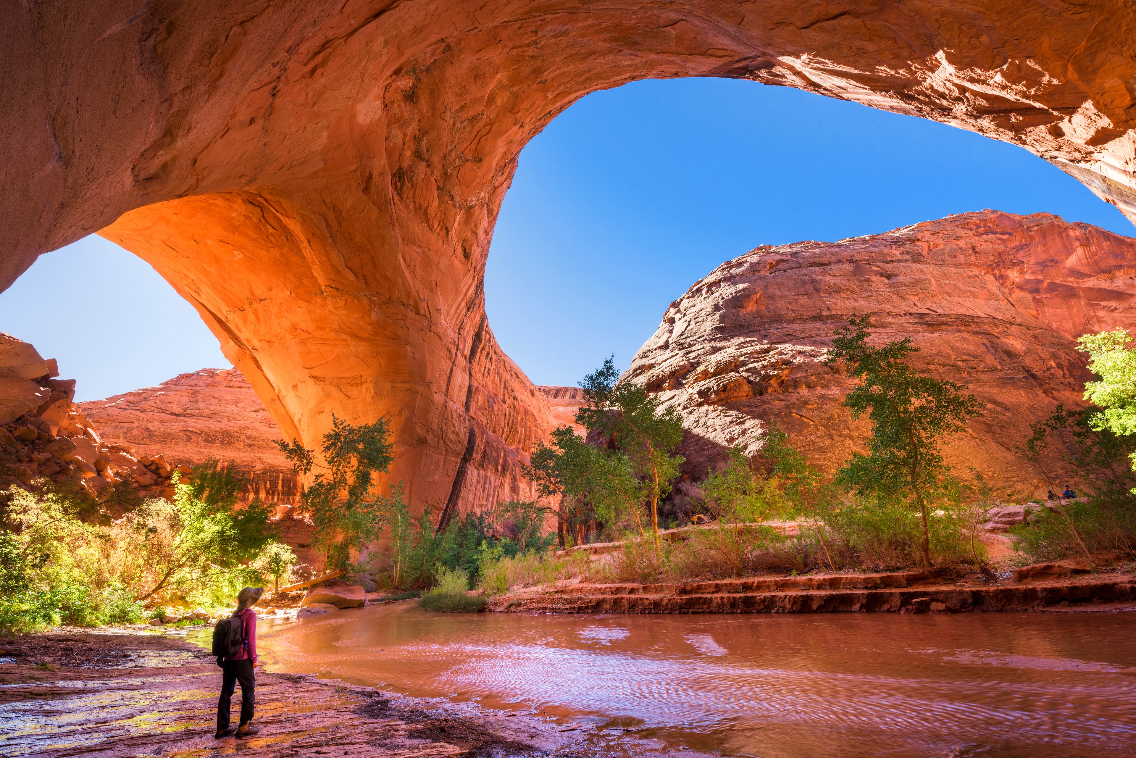 A hiker stands underneath Jacob Hamblin Arch in Coyote Gulch, Grand Staircase-Escalante National Monument, Utah, United States