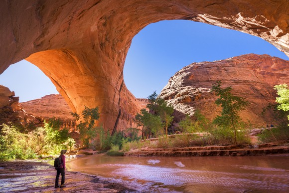 A hiker stands underneath Jacob Hamblin Arch in Coyote Gulch, Grand Staircase-Escalante National Monument, Utah, United States