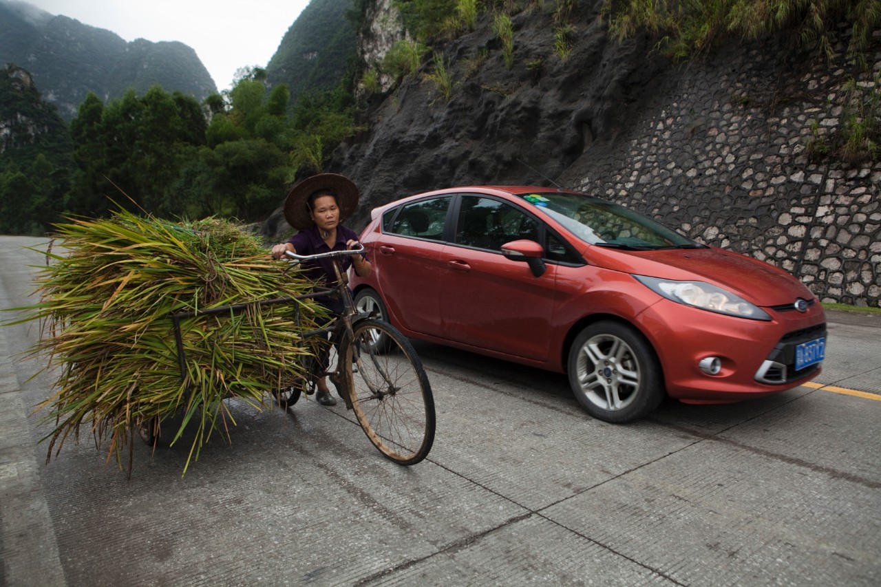Ford's Fiesta on a mountain-lined street in China, driving alongside a cyclist 