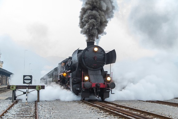 A locomotive chugging down the tracks, with steam pouring out.