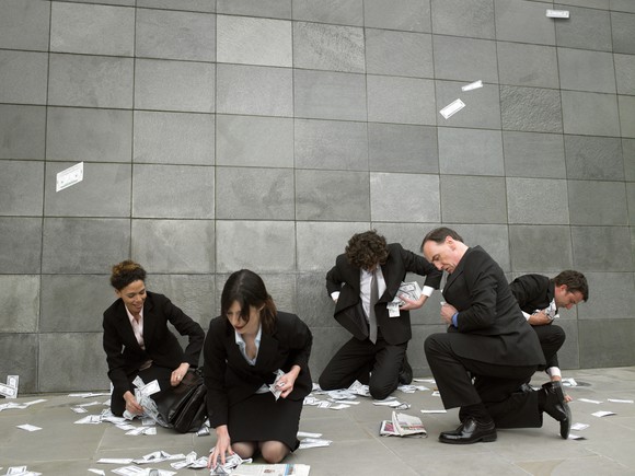 Five businesspeople bending down to pick up money off the floor of an office building 