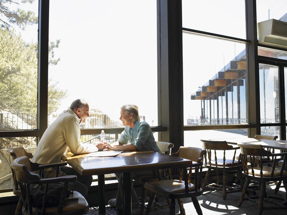 A retired couple holding hands in a restaurant.