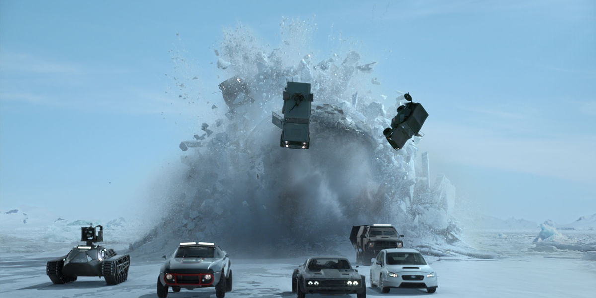 A fleet of vehicles racing on a snow surface, with an explosion in the background sending cars and snow flying in the air.