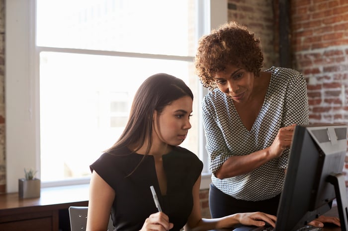 Two women work on a computer in a modern office space.