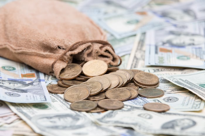 Gold coins spill out of a bag onto dollar bills.