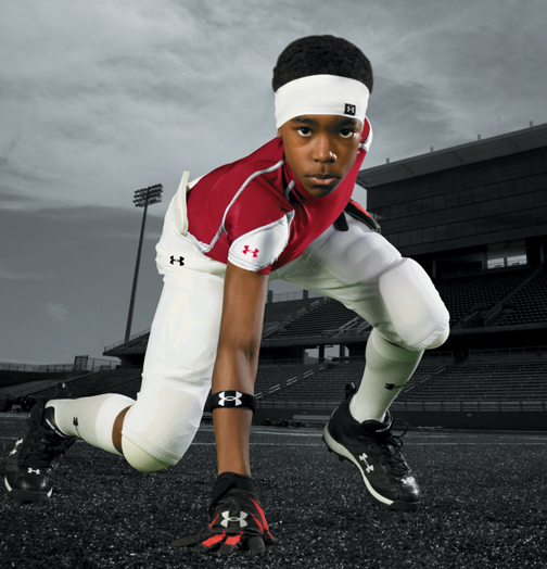 A boy football player in a starting position wearing Under Armour gear.