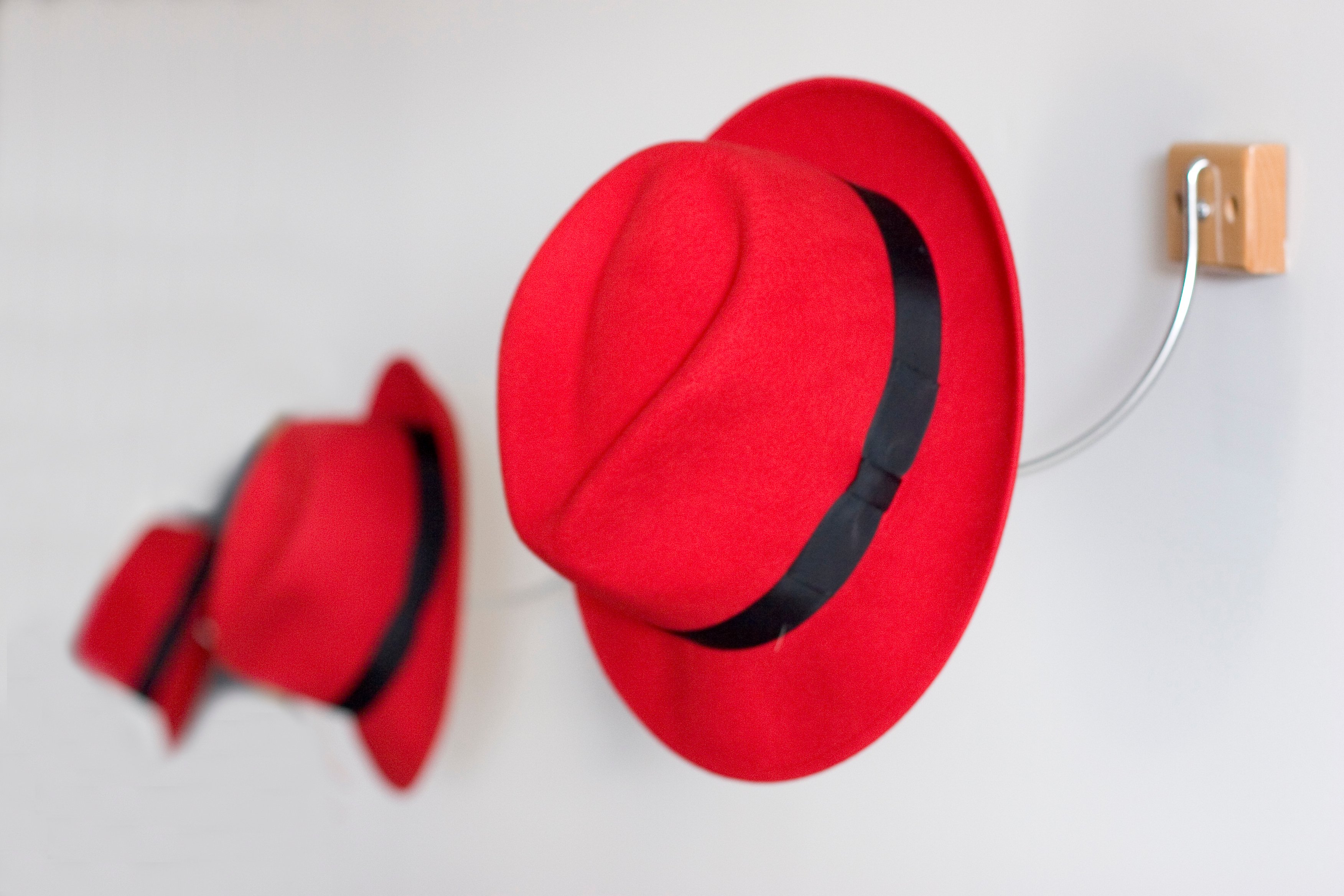 A line of red fedoras, hanging on wall hooks.
