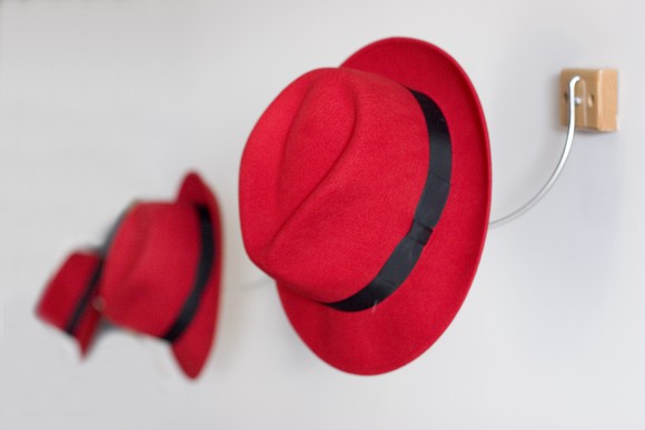 A line of red fedoras, hanging on wall hooks.