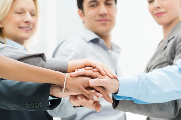 Five people in business attire putting their hands on top of one another in the middle of the group.