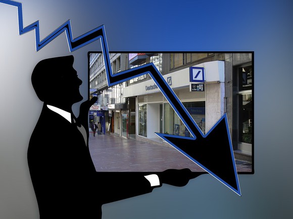 Silhouette of man standing in front of Deutsche Bank with arrow pointing down.