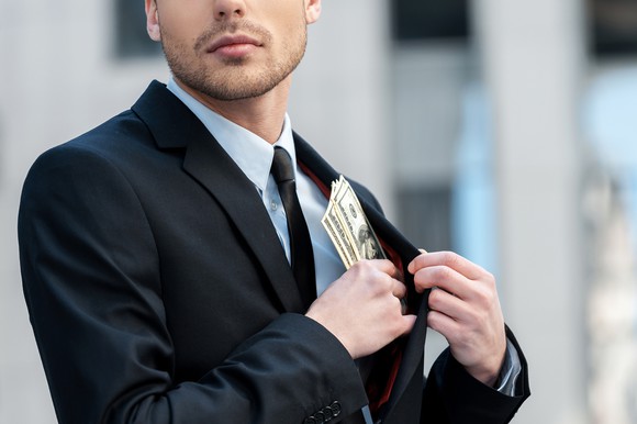 Man in suit stashing cash in coat pocket. 