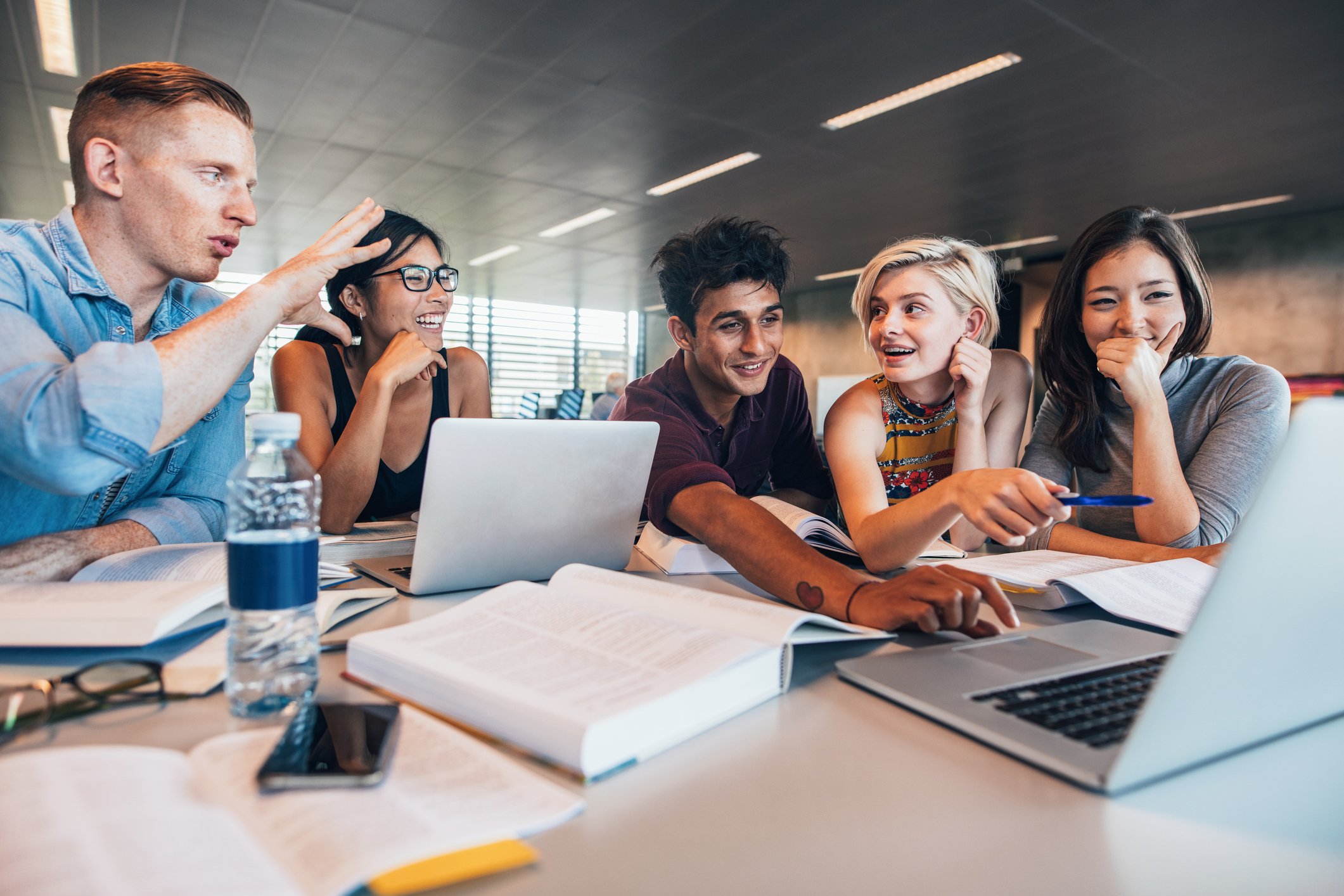Group of college students around a table, working on computers.