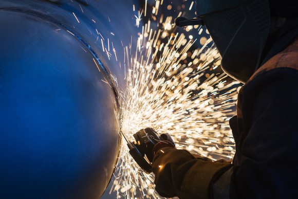 A worker uses a grinder on a welded steel tube. 