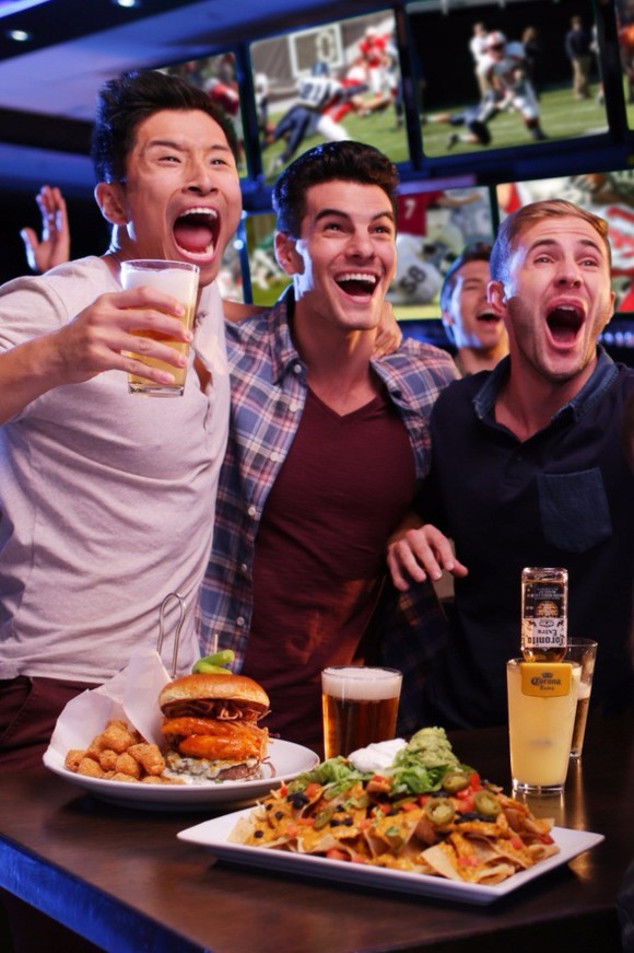 A group of guys watching a game and drinking beers at a Dave & Buster's.