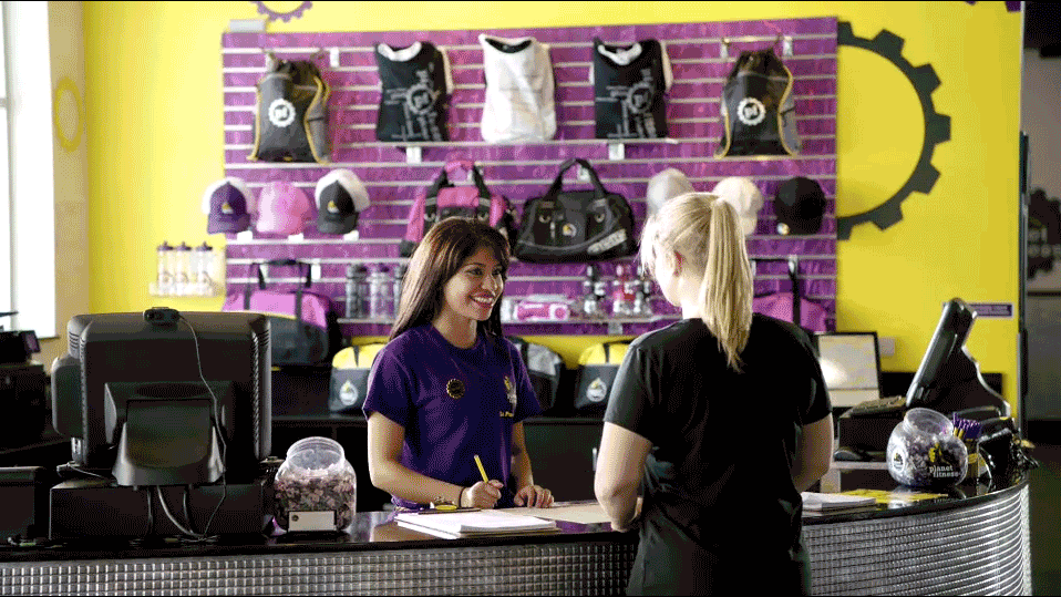 A woman behind the check-in counter at Planet Fitness helps a customer.