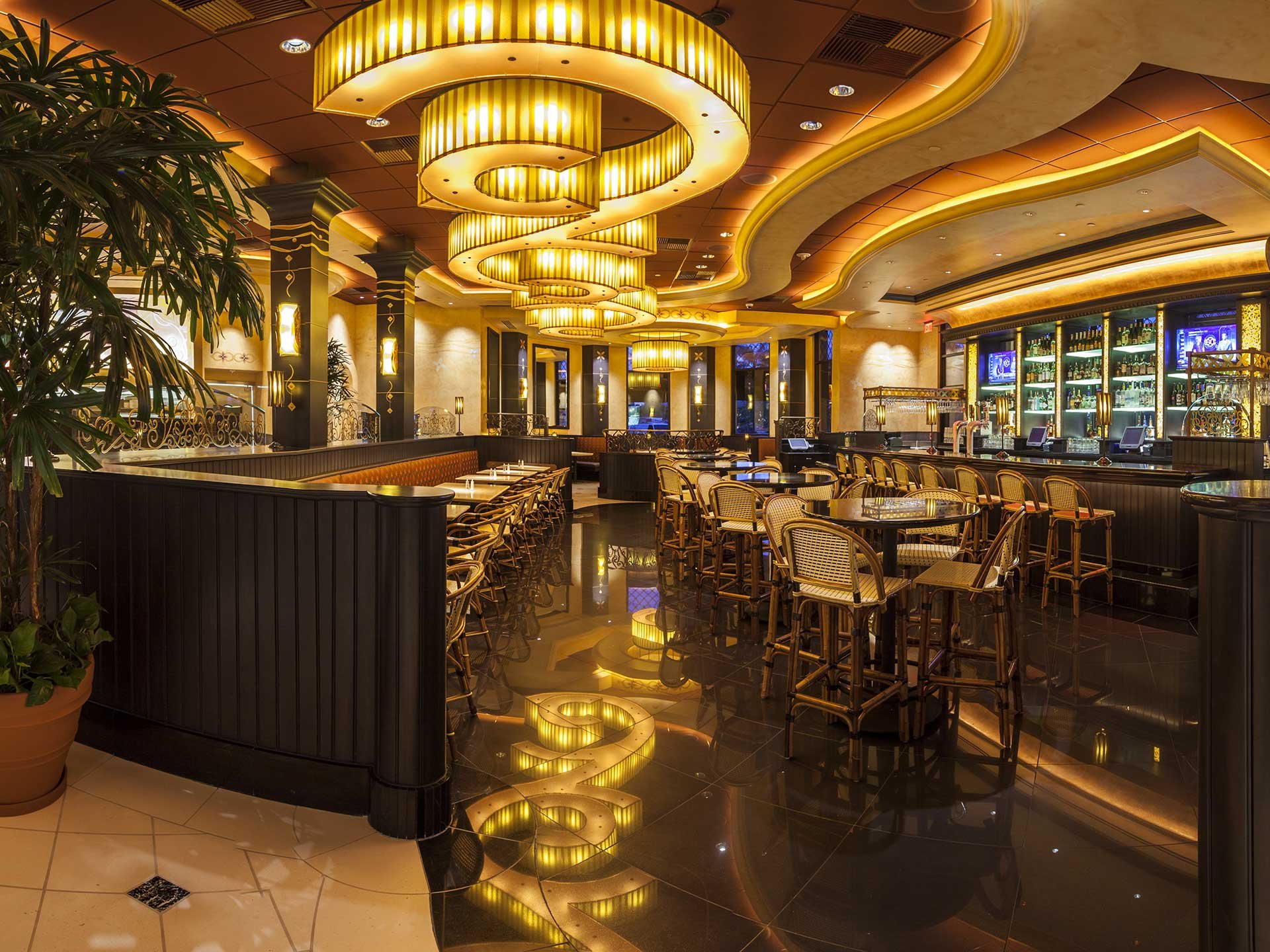 The interior of a Cheesecake Factory. The décor is art-deco, dark colors and swirling lights reminiscent of the pre-war era.