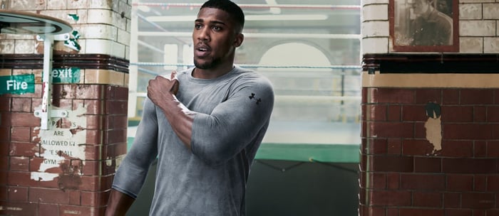 An athlete wears a grey Under Armour shirt while stretching at a gym.