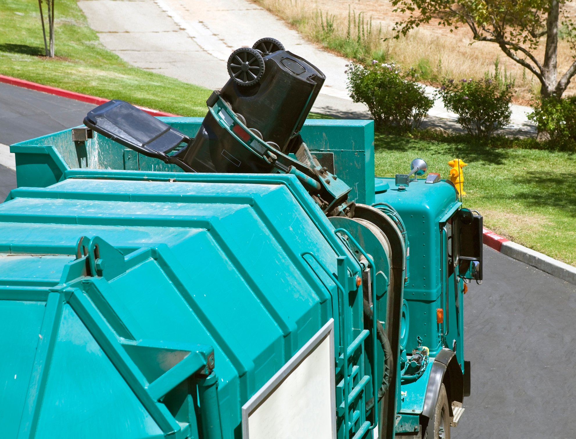Robotic arm trash truck dumps a large black can.