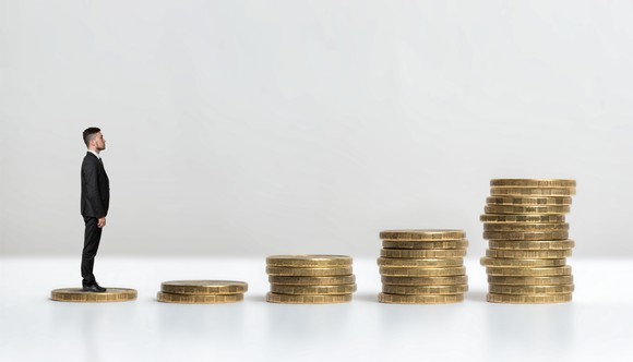 Man standing on small stack of coins, looking at increasingly larger stacks ahead.