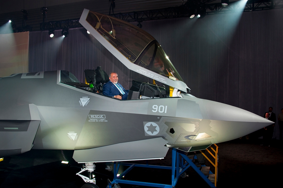 Israel's minister of defense smiling from the open cockpit of an F-35 on display.
