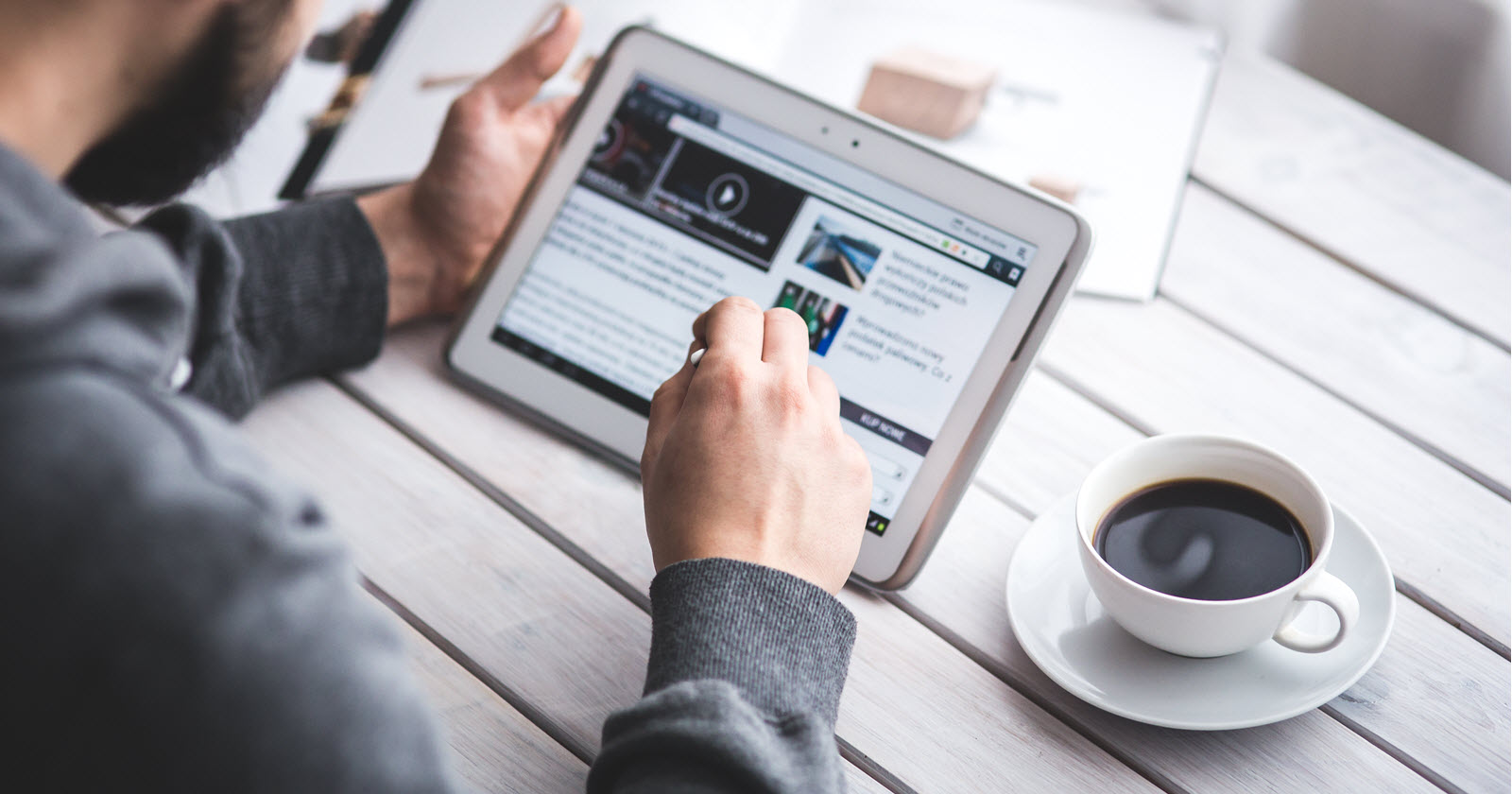 A man looks at a tablet computer. with a cup of coffee sitting next to him on a table.