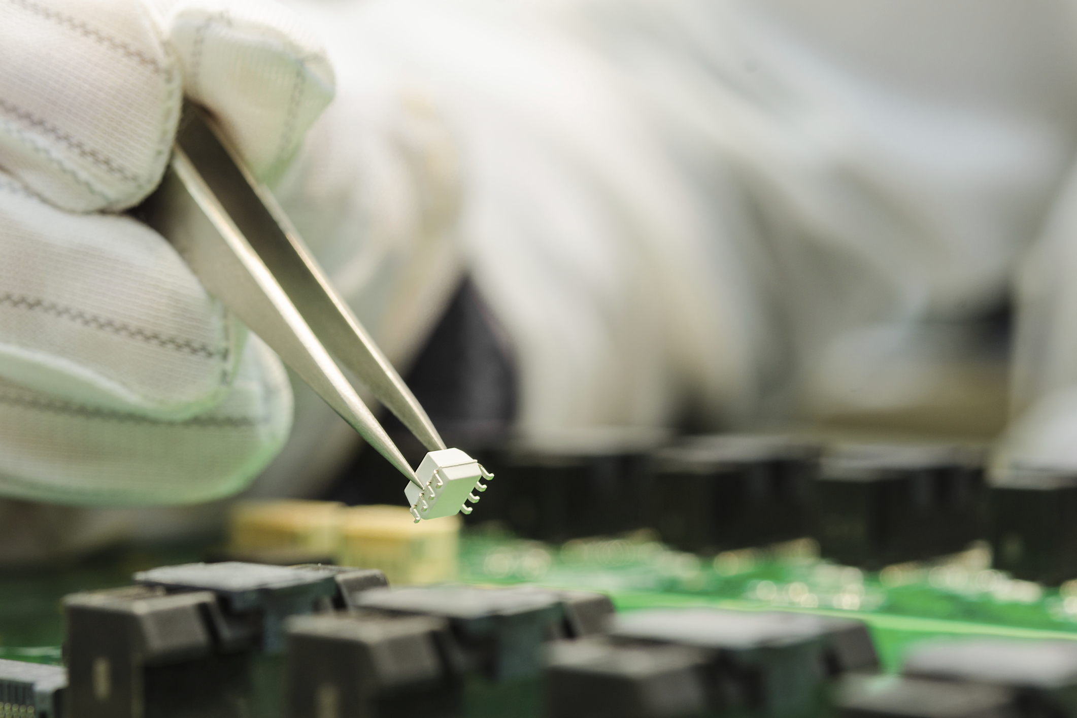 A gloved worker installs a chip onto a circuit board.