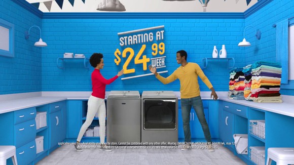A couple stands in front of rented appliances in front of a sign that says "starting at $24.99 per week"