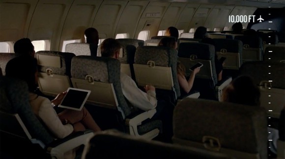 A airplane cabin with various people connected to their devices and text saying "10,000 feet"