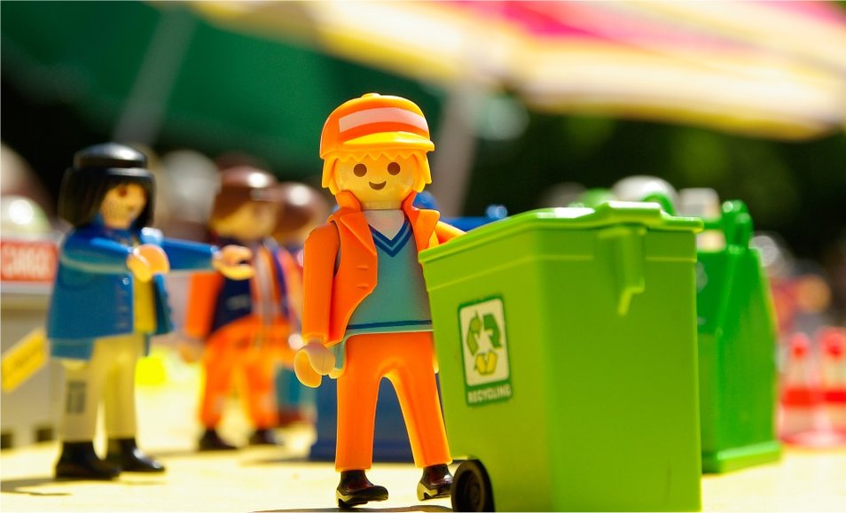 A Lego figure pushing a recycling bin.