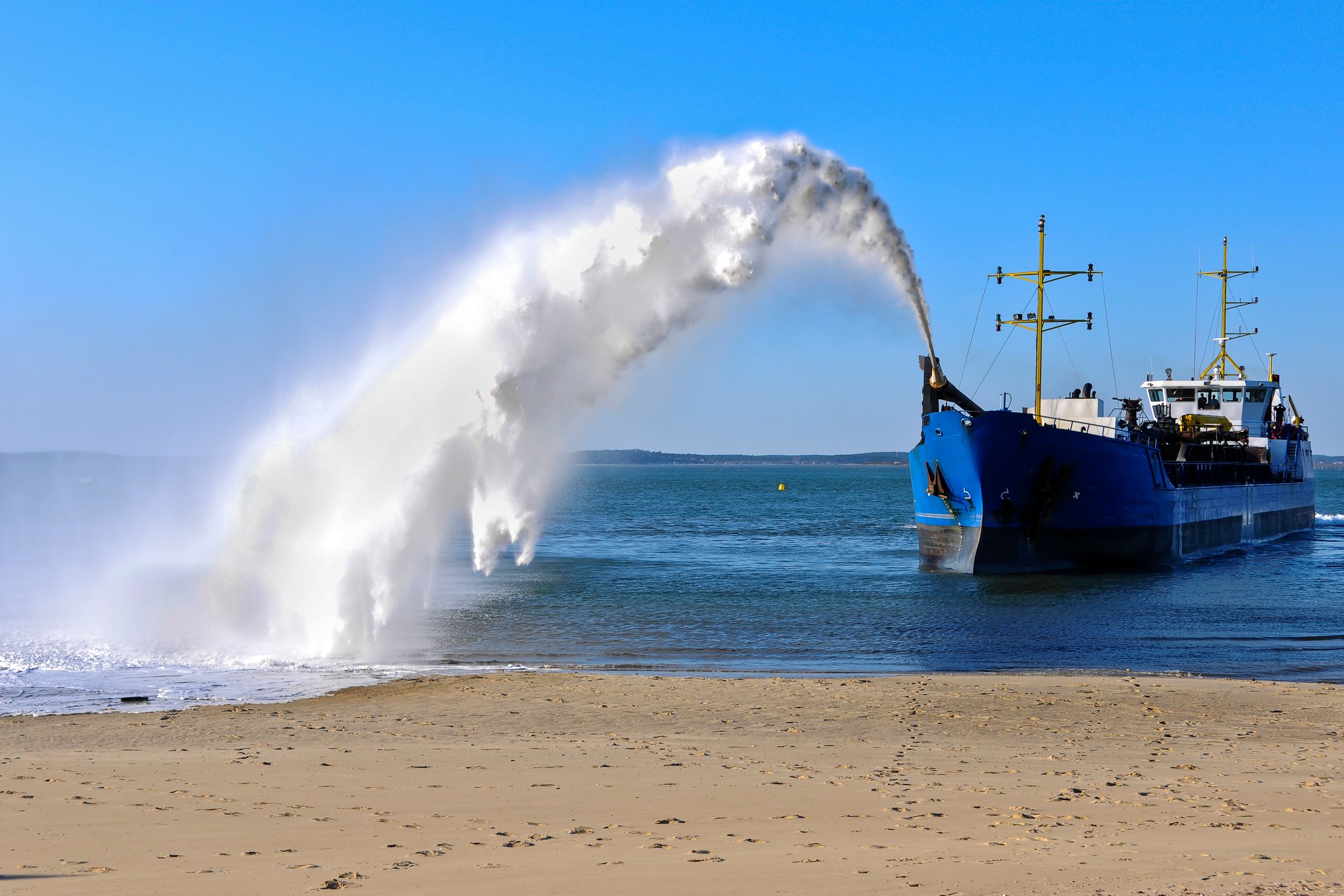 Dredging ship spraying sand onto shore.