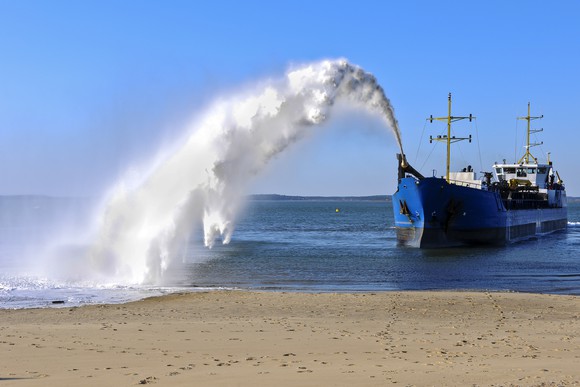 Dredging ship spraying sand onto shore.