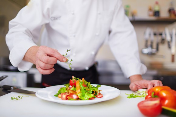 A chef adding herbs to a salad.