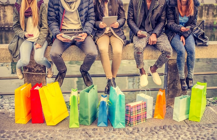 Five people sitting on a bridge with shopping bags nearby