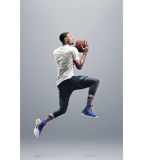 Steph Curry in casual-looking but athletic clothing jumping with a basketball.