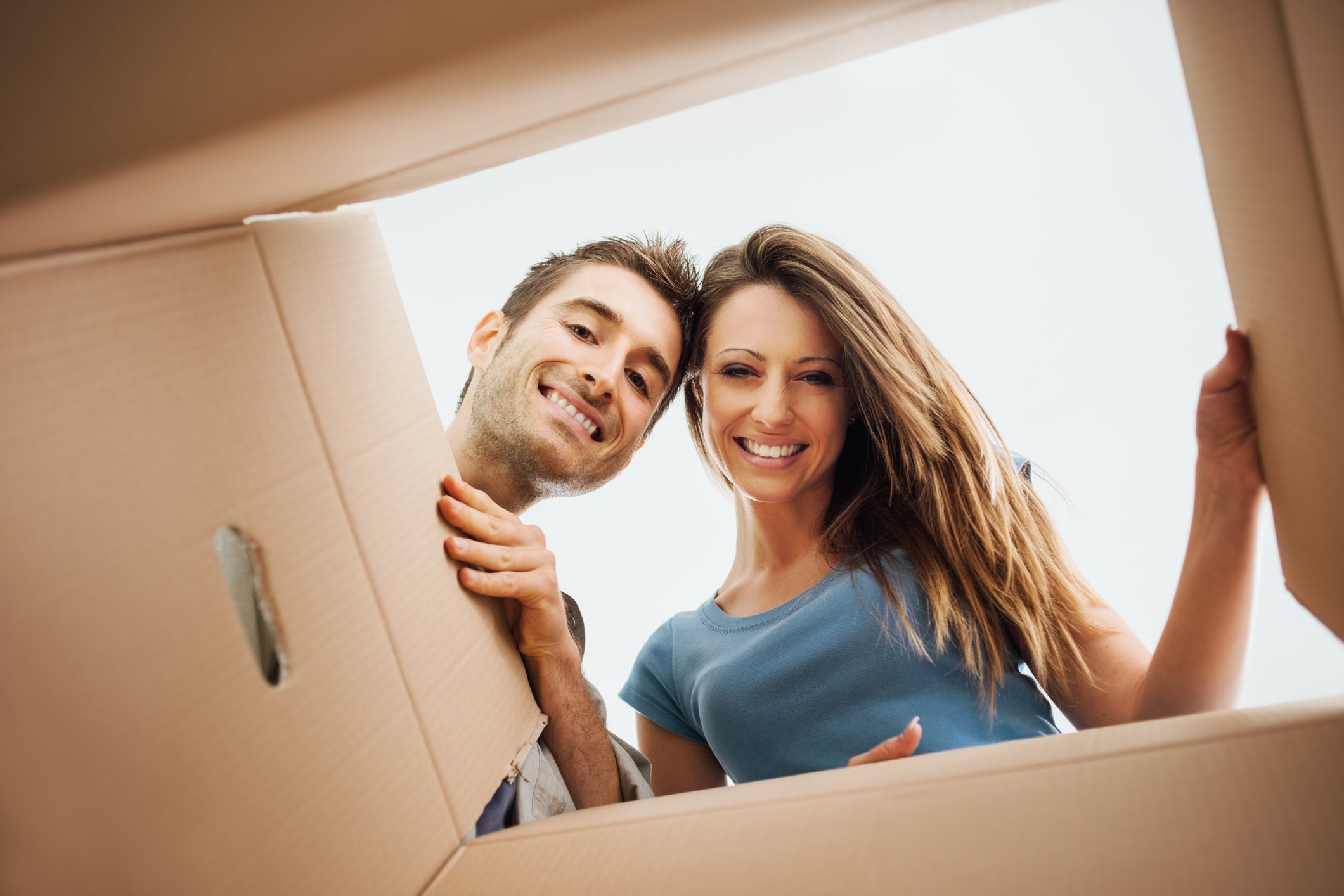 A man and woman peer happily into a cardboard package delivery.