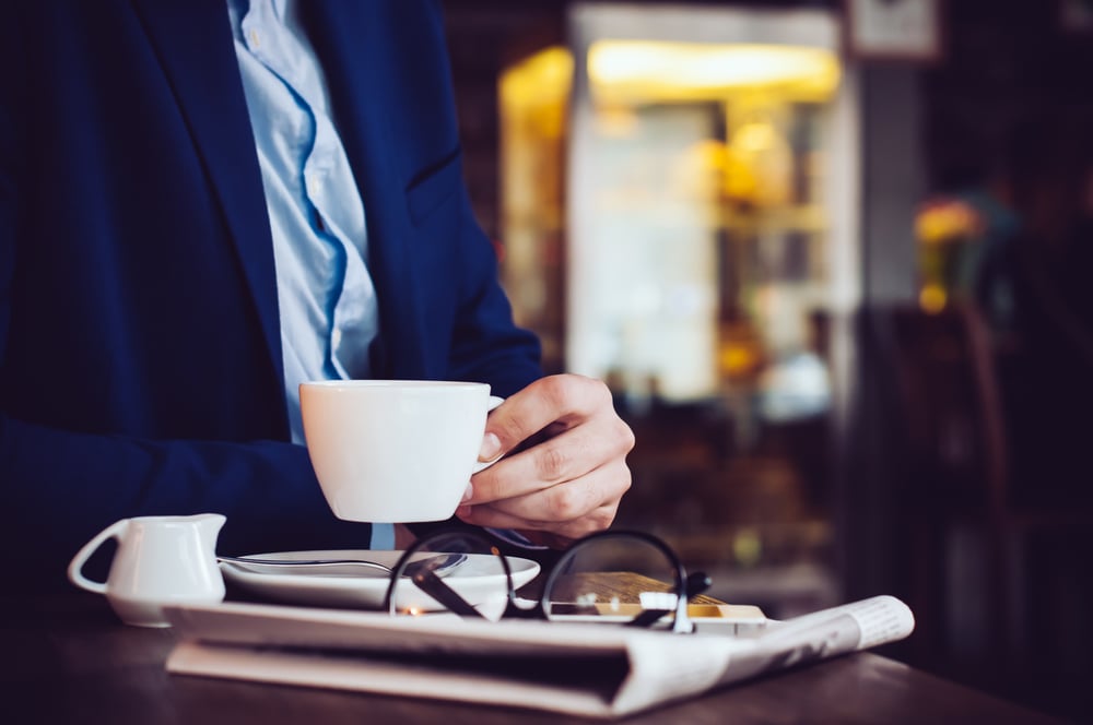 Business man drinking coffee with folded newspaper.