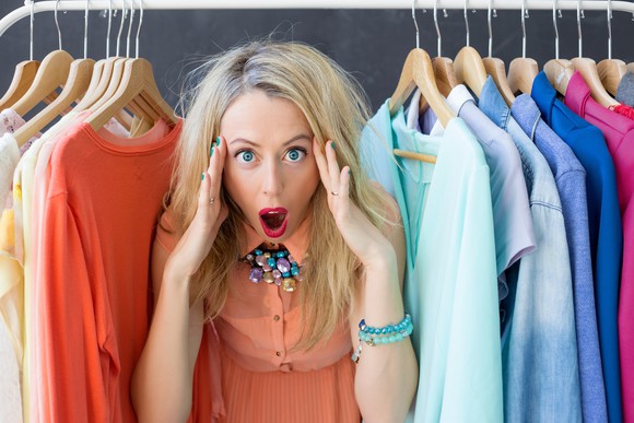 A surprised woman standing in the middle of a row of clothes.