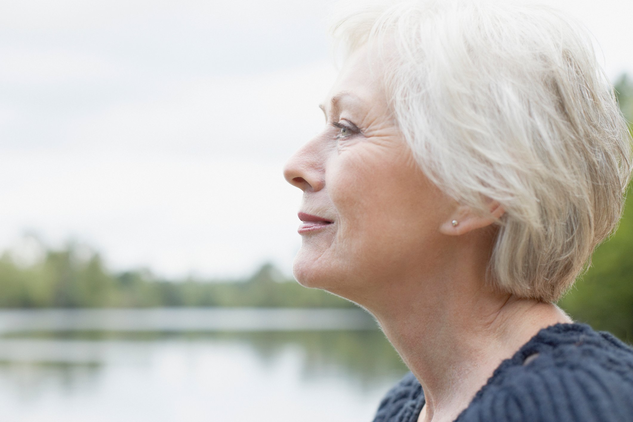 Side profile of an older woman, smiling, as she stands by the water.