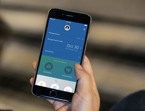 Woman holding smartphone with PayPal app open.