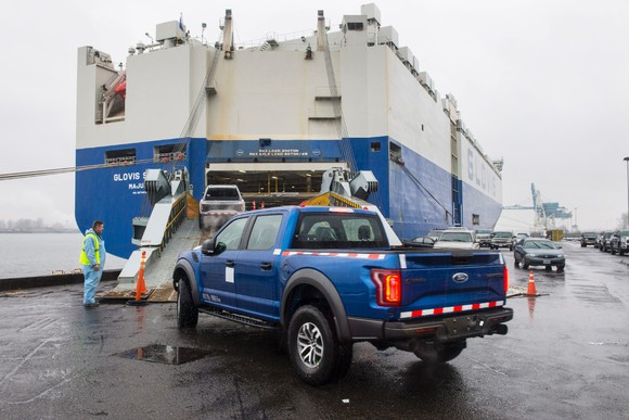 A blue Ford F-150 Raptor being loaded onto a cargo ship.