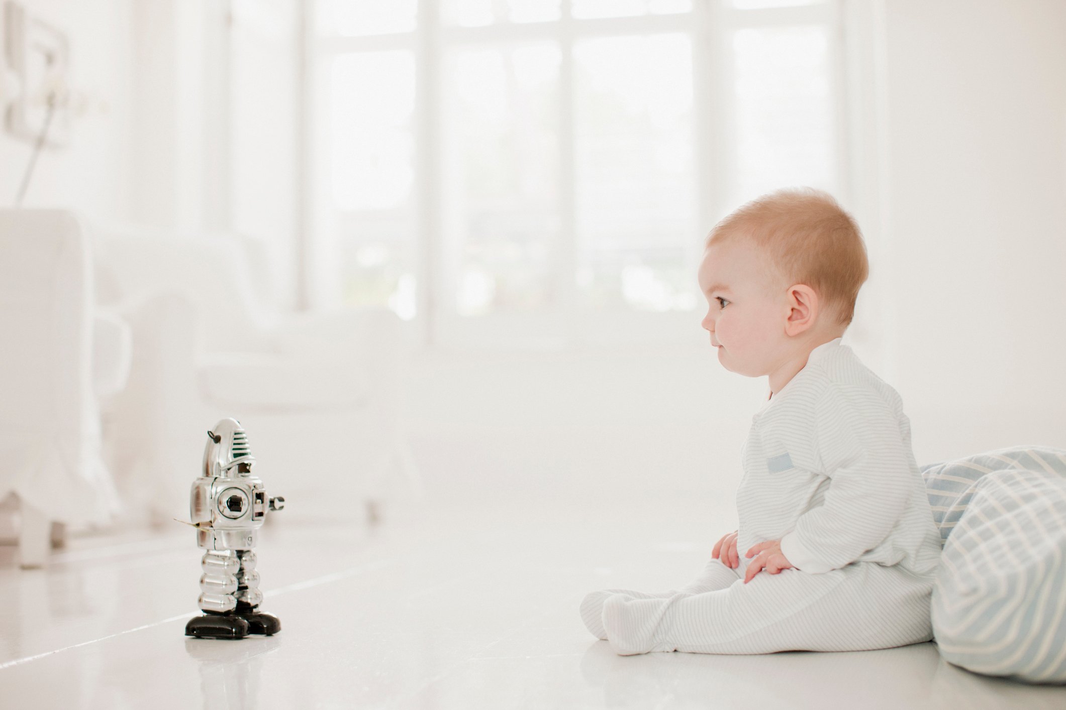 A baby sitting next to a toy robot.