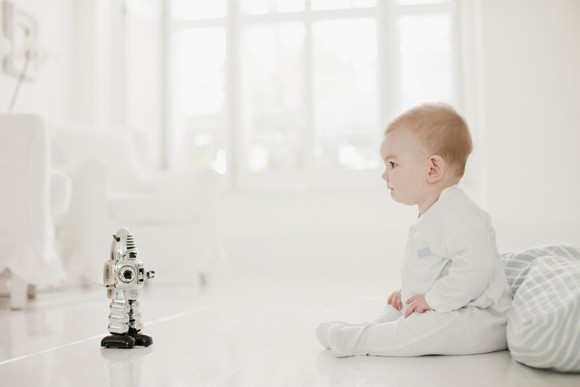 A baby sitting next to a toy robot.