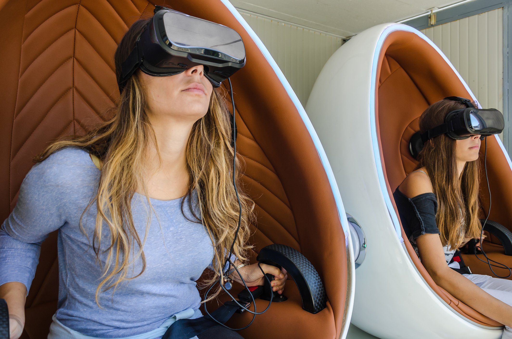Two women sitting in pods with virtual-reality headsets on.