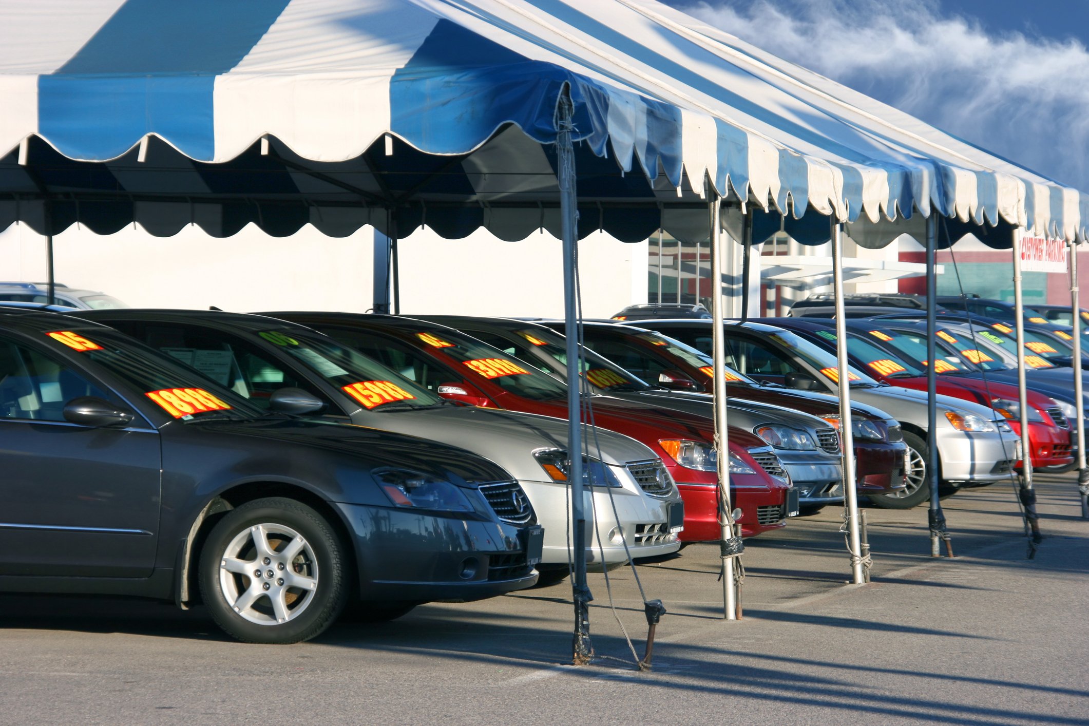 Row of cars under an awning at a dealership.