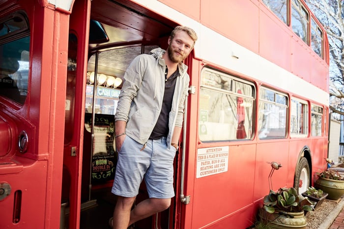 A man stands in the doorway of a bus wearing fashionable Abercrombie clothing. 