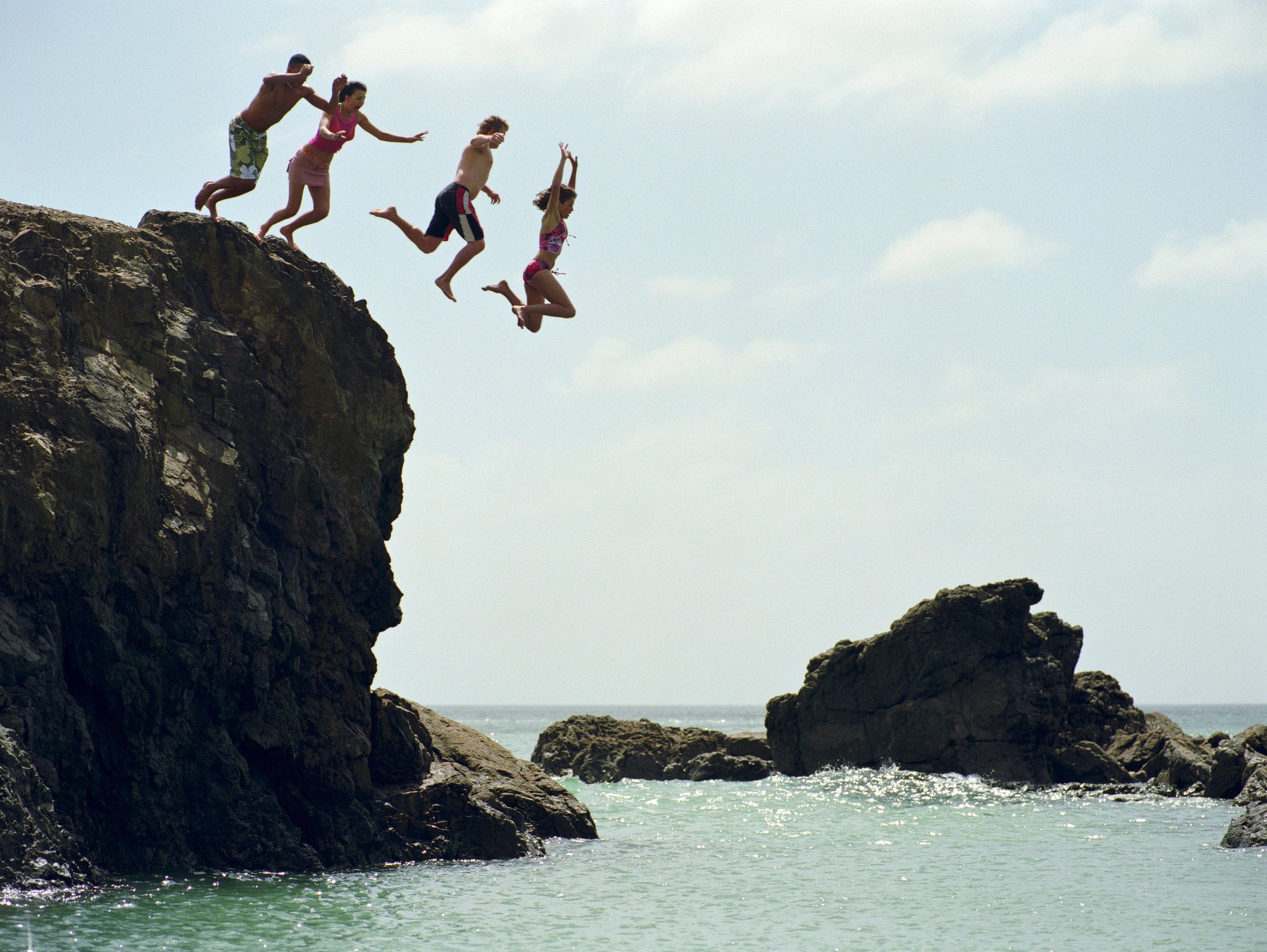 Four people jumping off a short cliff and into water.