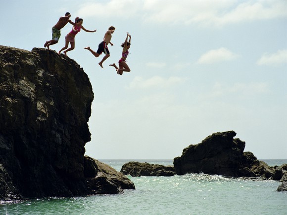 Four people jumping off a short cliff and into water.