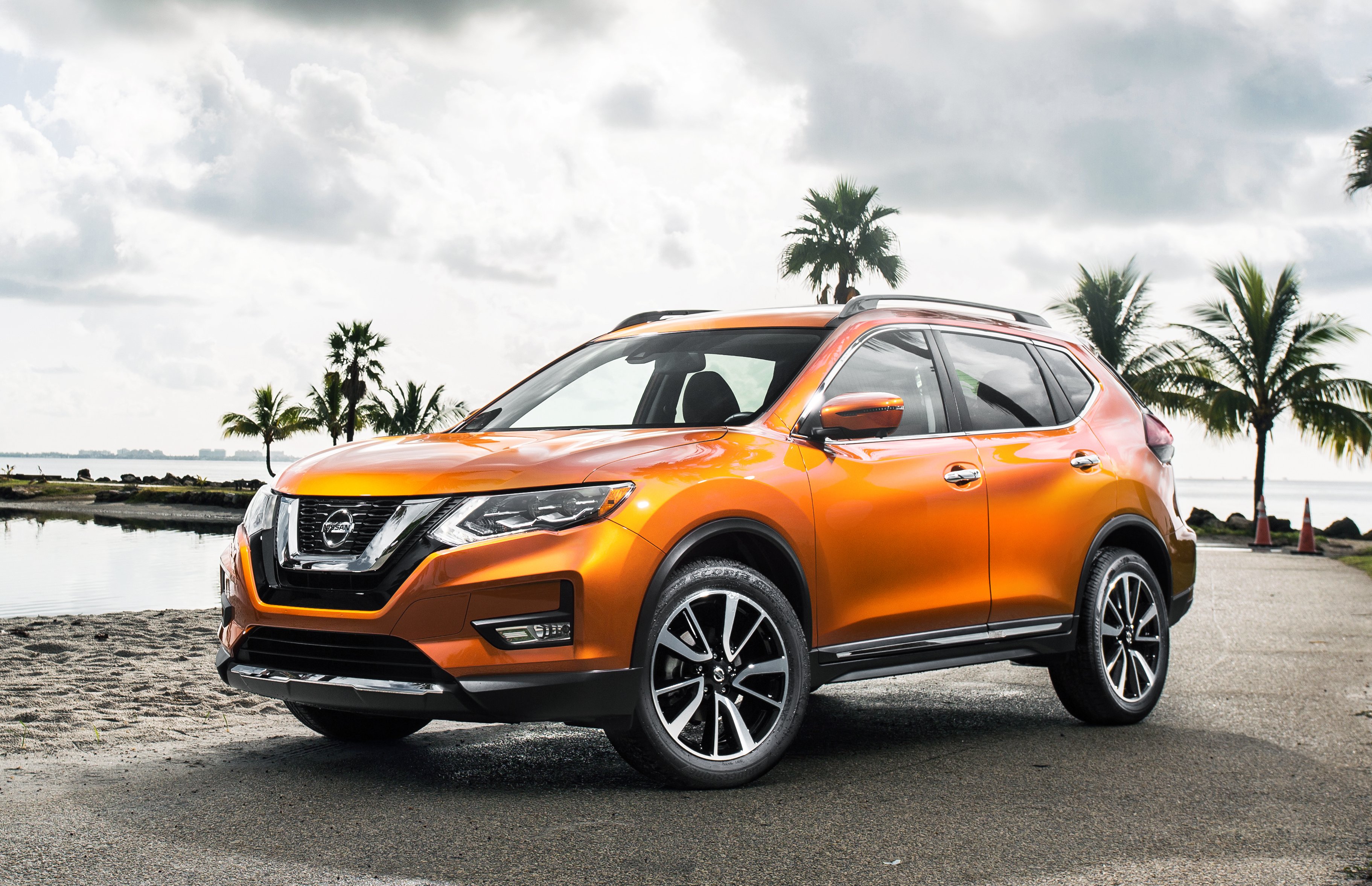An orange Rogue SUV in a tropical waterfront setting