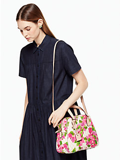 A woman in a black dress wearing a Kate Spade purse, done in white and decorated with pink floral print.