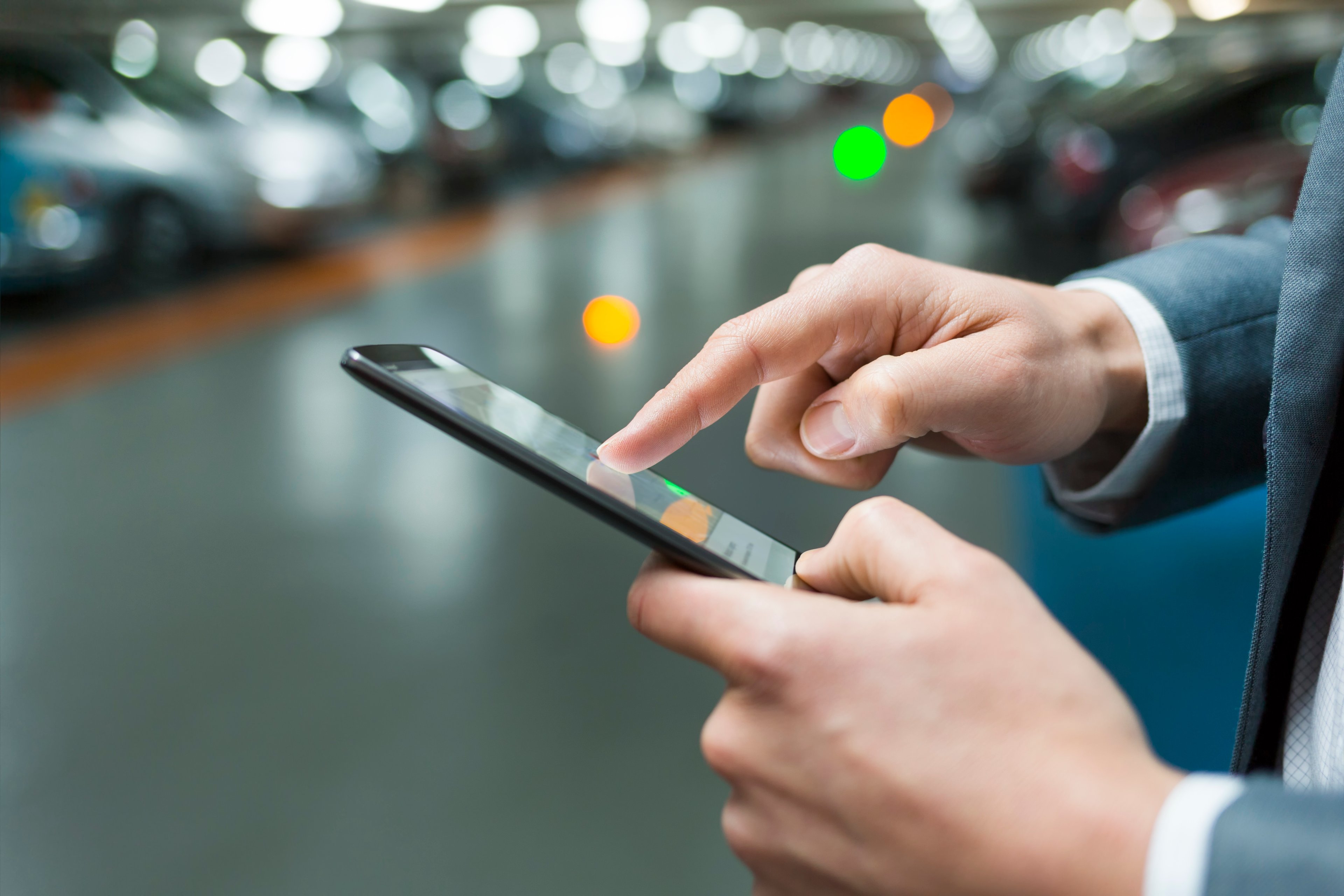 Close-up of a man's hands using  a cell phone in a parking lot. 